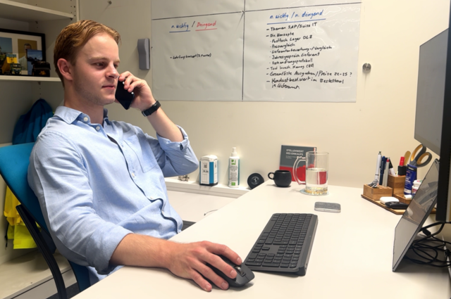 Julian arbeitet an seinem Laptop und telefoniert in seinem Büro
