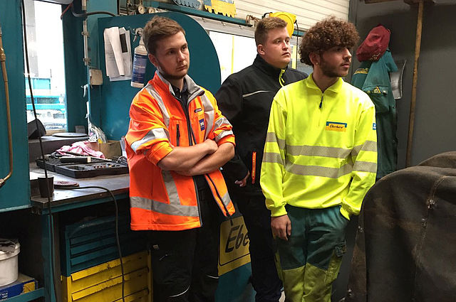 Drei junge Männer stehen in der Werkstatt und blicken auf etwas.